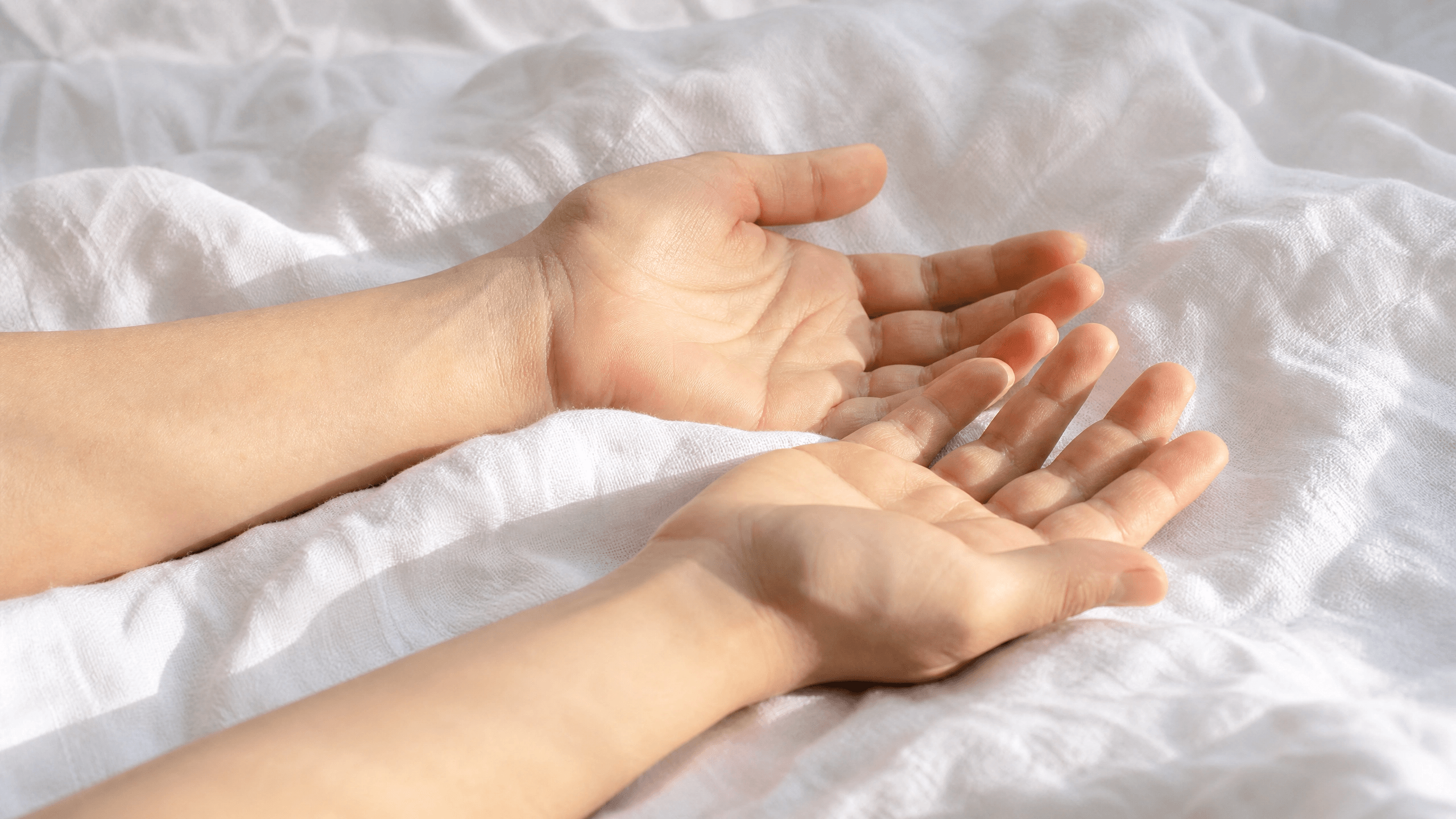 Mãos abertas e relaxadas sobre tecido claro em postura de entrega e descanso espiritual